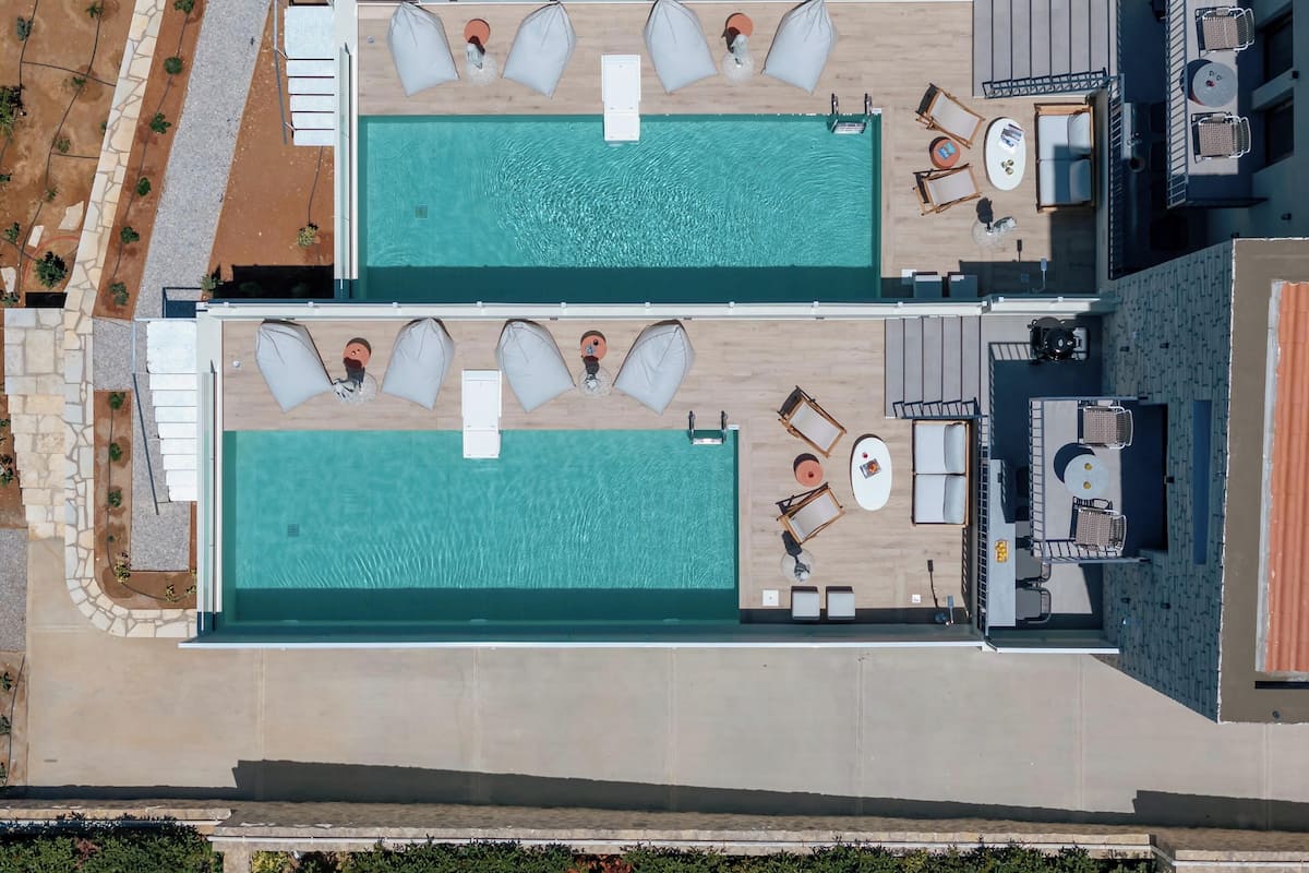 An aerial view of a hotel with two swimming pools, lounge areas with sunbeds, and a small bar area.