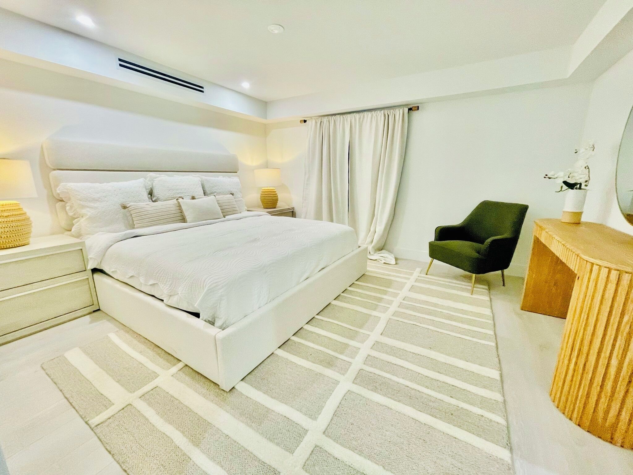A modern bedroom with a large bed, a bedside table, a chair, and a vanity with a mirror.