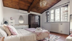 A bedroom with a wooden ceiling, a bed with pink and white bedding, a dresser, a mirror, and a window with decorative glass panes. - IL CASTELLETTO (Grottaferrata)