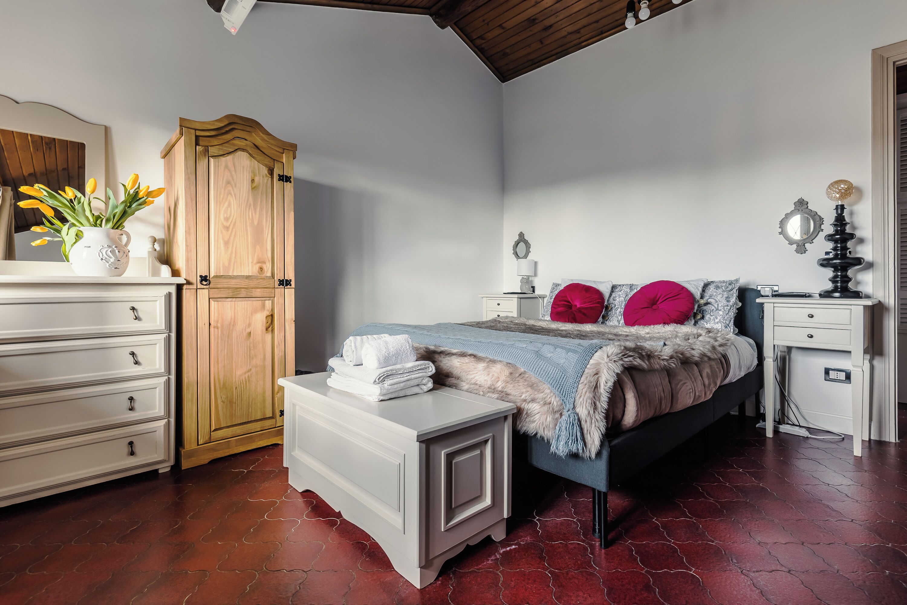 Un dormitorio con cama, un armario de madera, un tocador blanco y una mesita de noche con lámpara.