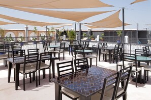 Un patio al aire libre con varias mesas y sillas, cubierto por grandes sombrillas, rodeado por una cerca decorativa.