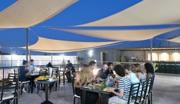 An outdoor dining area with tables and chairs under large canopies, a bar area in the background, and a clear sky. - The Central House Marrakech Medina (Marrakech)
