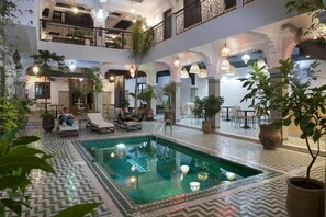 A multi-level indoor pool area with lounge chairs, potted plants, and hanging lights. - The Central House Marrakech Medina (Marrakech)