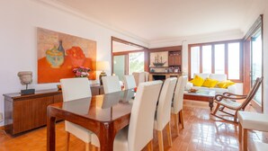 A dining area with a wooden table and chairs, a painting on the wall, and a view of the kitchen through an open doorway. - Ca n Quiros in Mallorca (Santa Margalida)