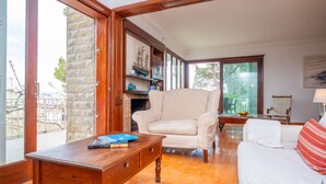 A spacious living room with a white sofa, a wooden coffee table, and a white armchair. There is a bookshelf with decorative items and a window providing a view of the outdoors. - Ca n Quiros in Mallorca (Santa Margalida)