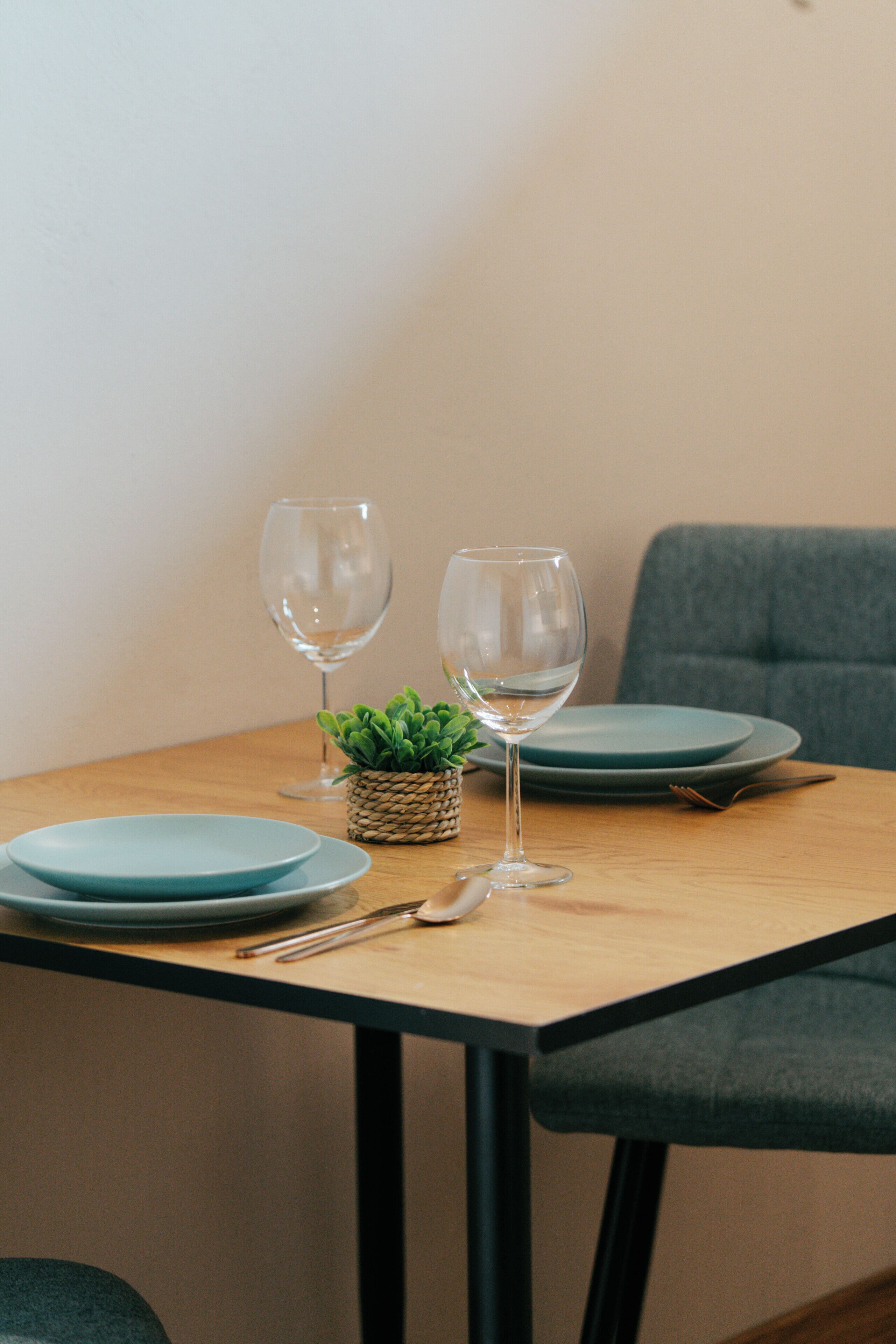 Een eettafel met twee borden, twee wijnglazen, een kleine plant en bestek.