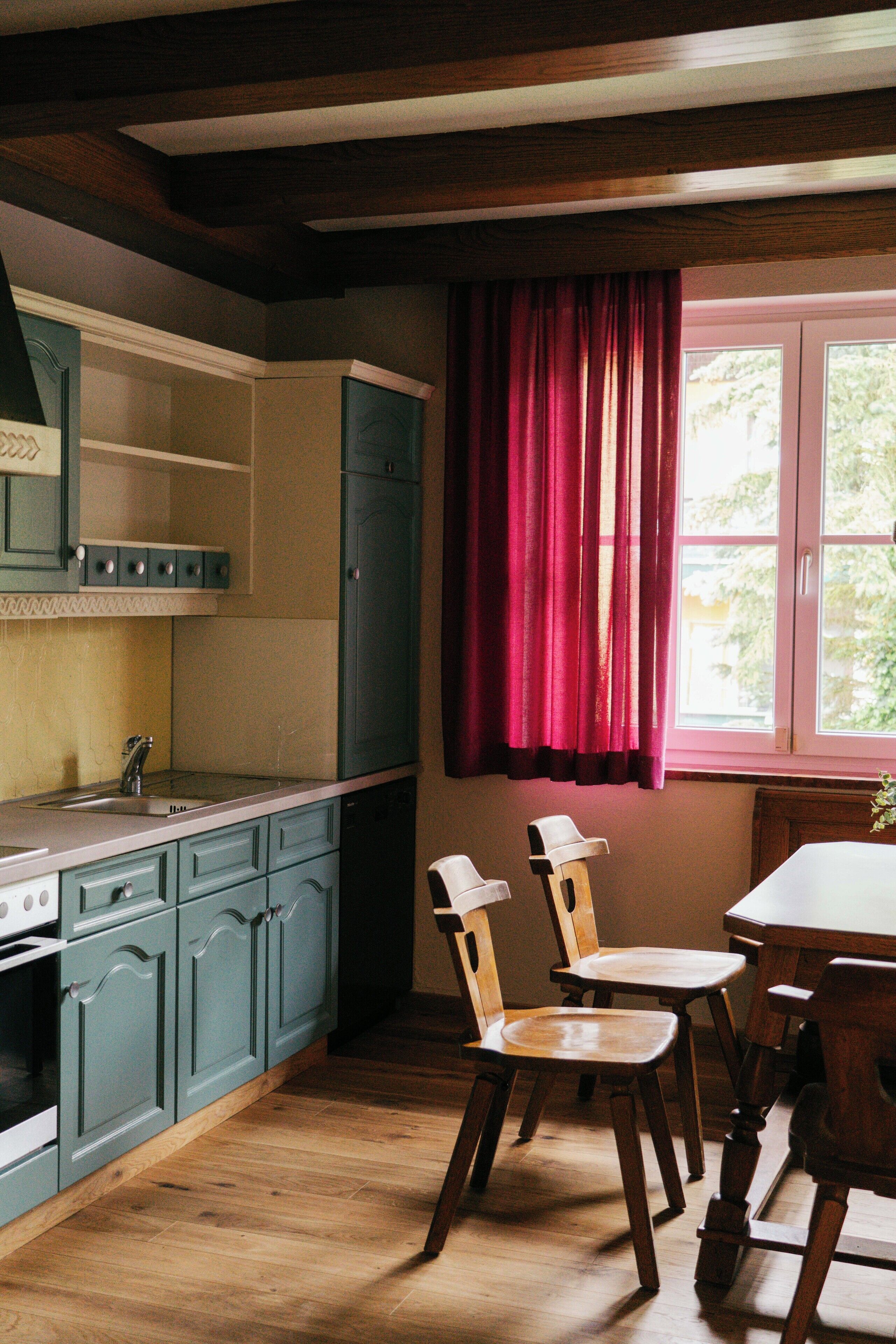 A kitchen with wooden cabinets, a dining table with chairs, and a window with curtains.