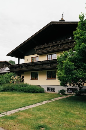 Ein traditionelles Gebäude mit einem geneigten Dach, mehreren Fenstern und einem kleinen Garten davor.