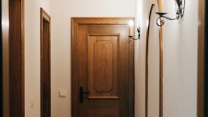 Un pasillo estrecho con suelo de madera, una puerta de madera y un aplique en la pared.