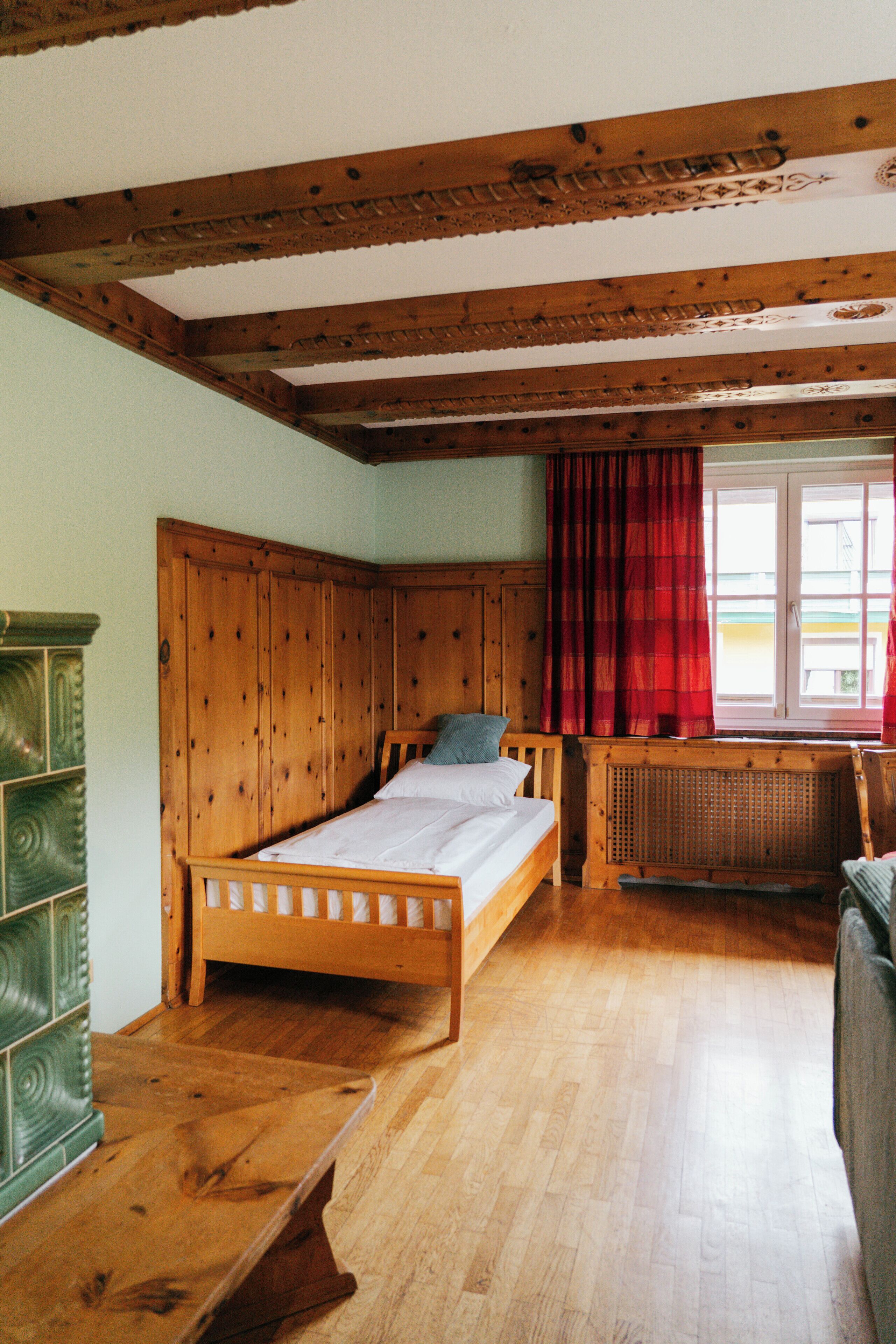 Een houten bed in een kamer met een raam, een radiator en een groene kast.
