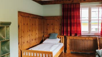 Een houten bed in een kamer met een raam, een radiator en een groene kast.