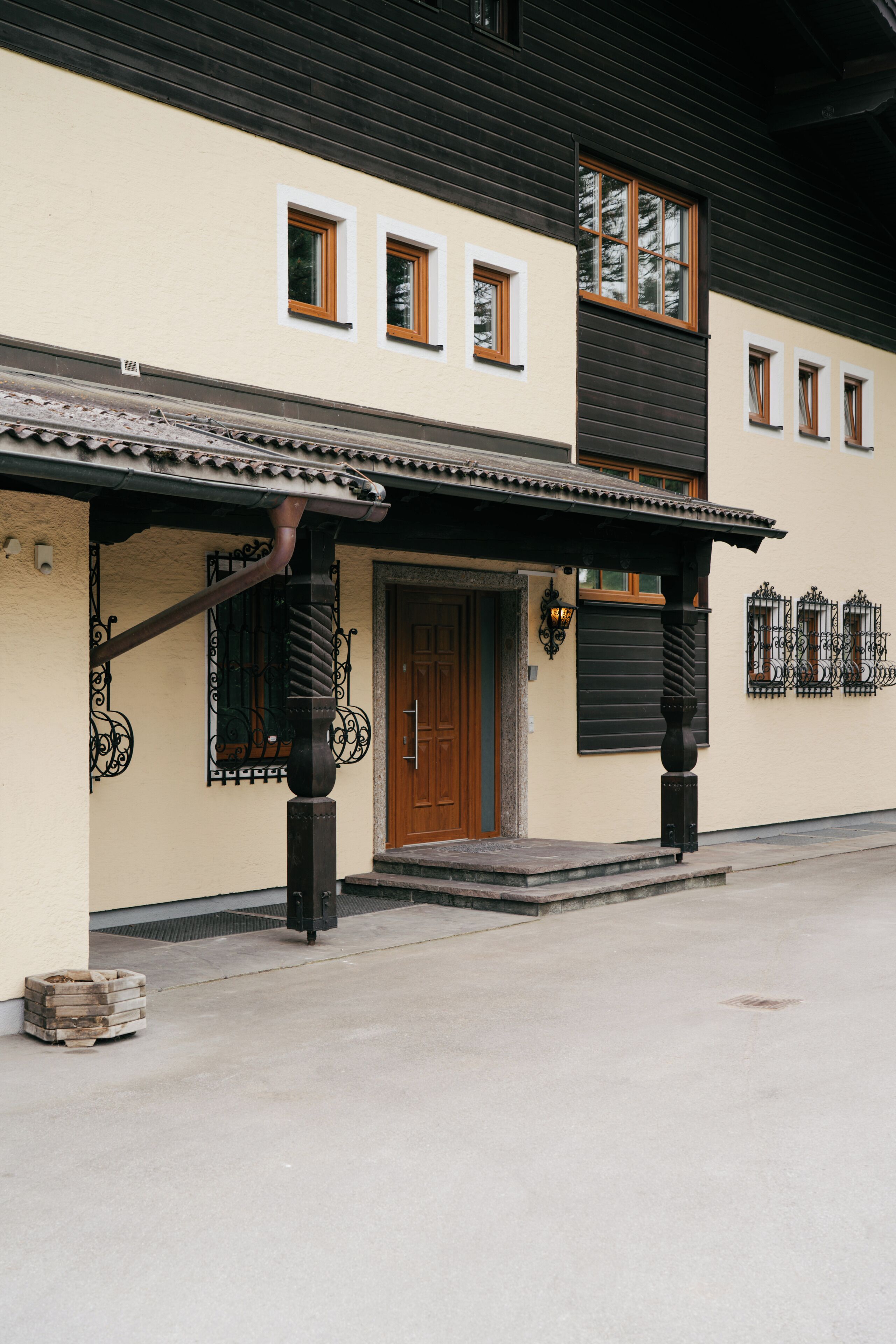 A building with a beige facade, a wooden door, and a covered entrance area with a tiled roof.