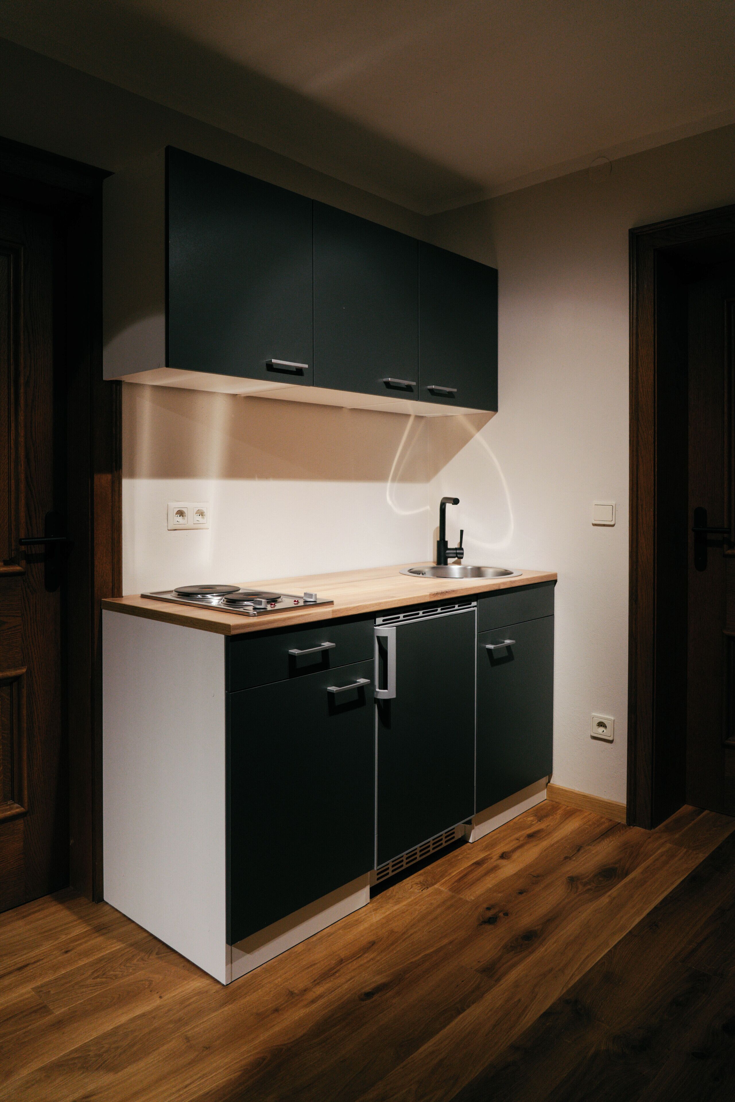 A compact kitchen with a wooden countertop, black cabinets, and a built-in dishwasher.