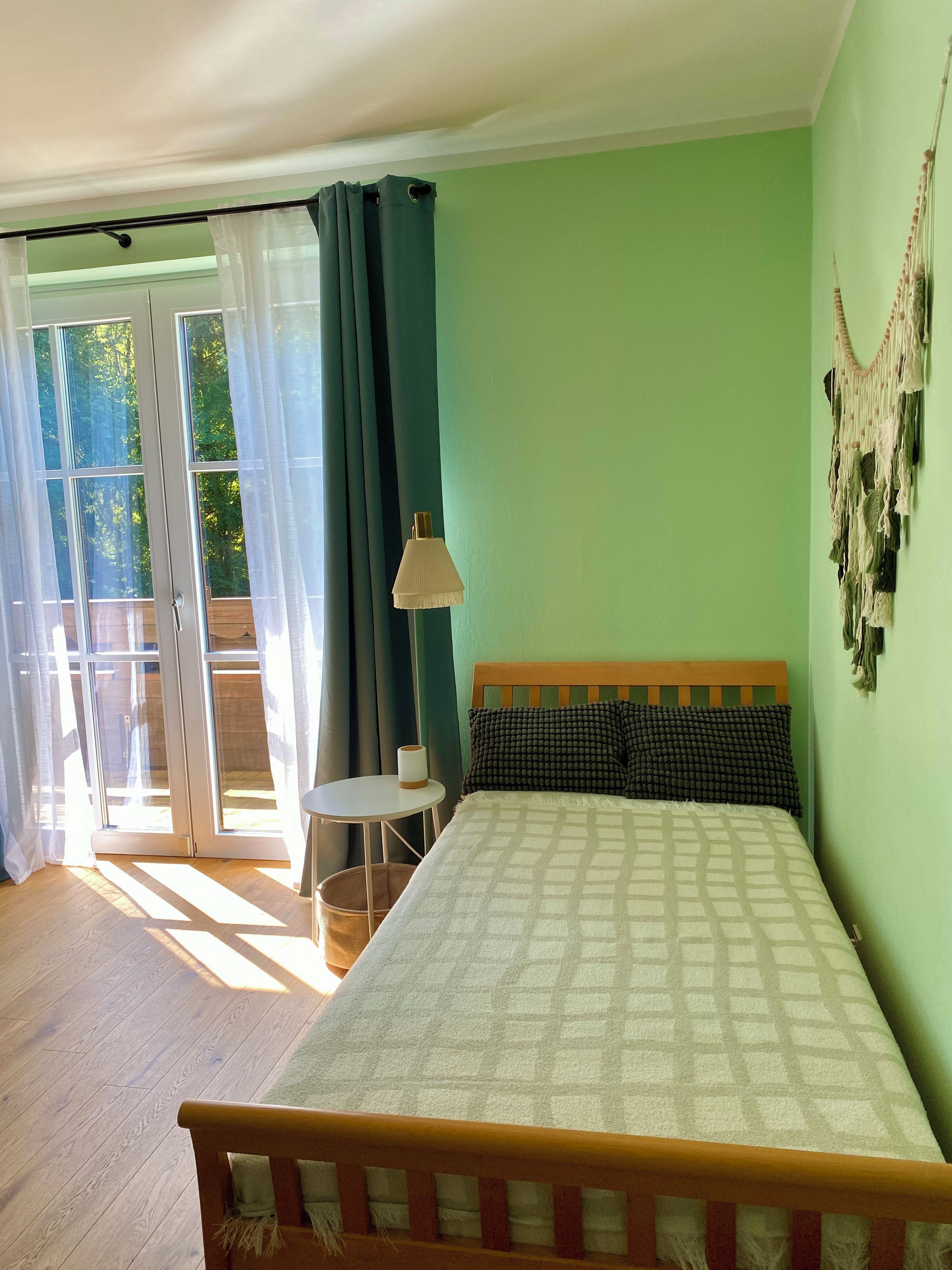 Un dormitorio con cama, mesita de noche, lámpara, ventana con cortinas y vistas al exterior.