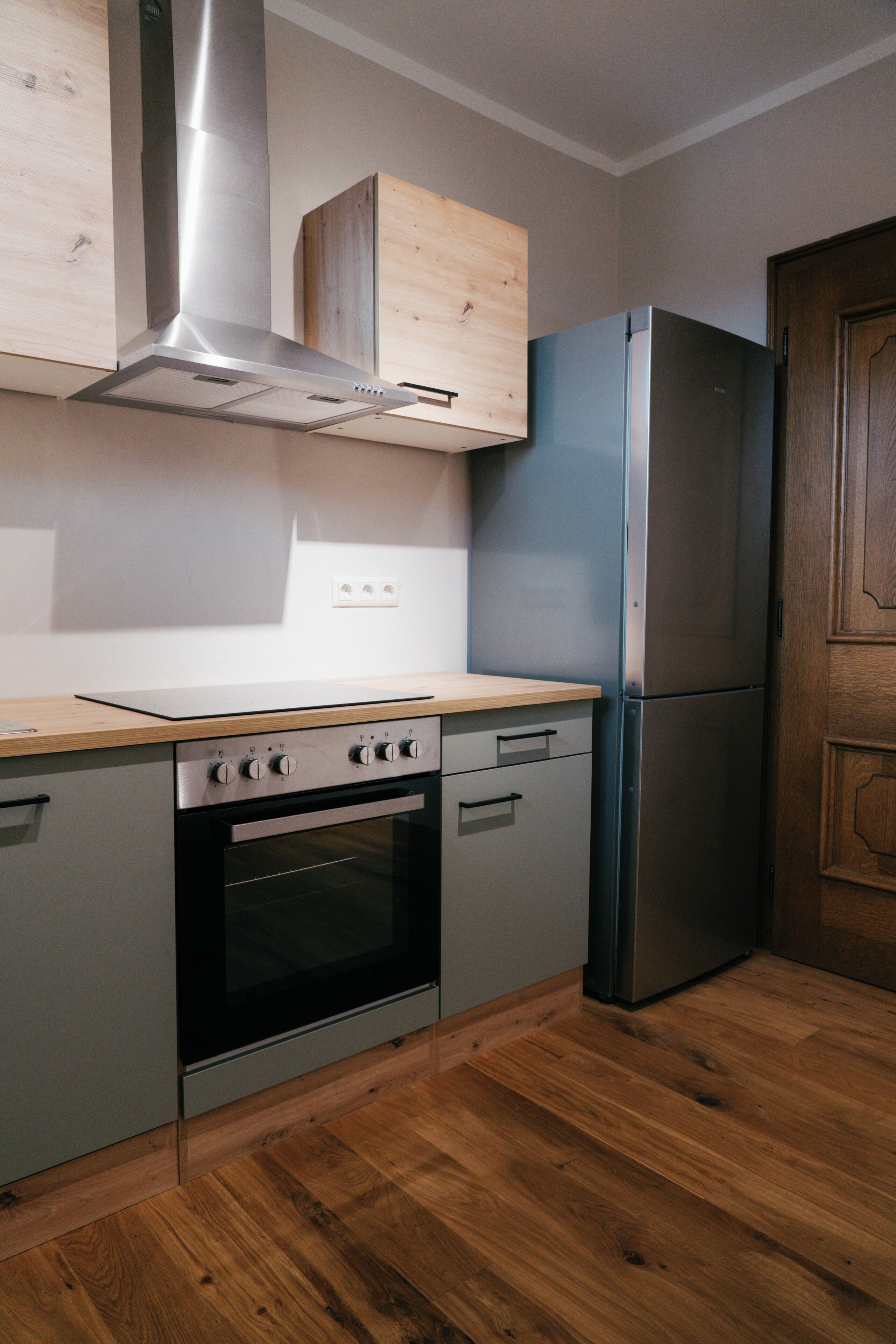 A kitchen with a stainless steel range hood, a built-in oven, a refrigerator, and wooden cabinets.