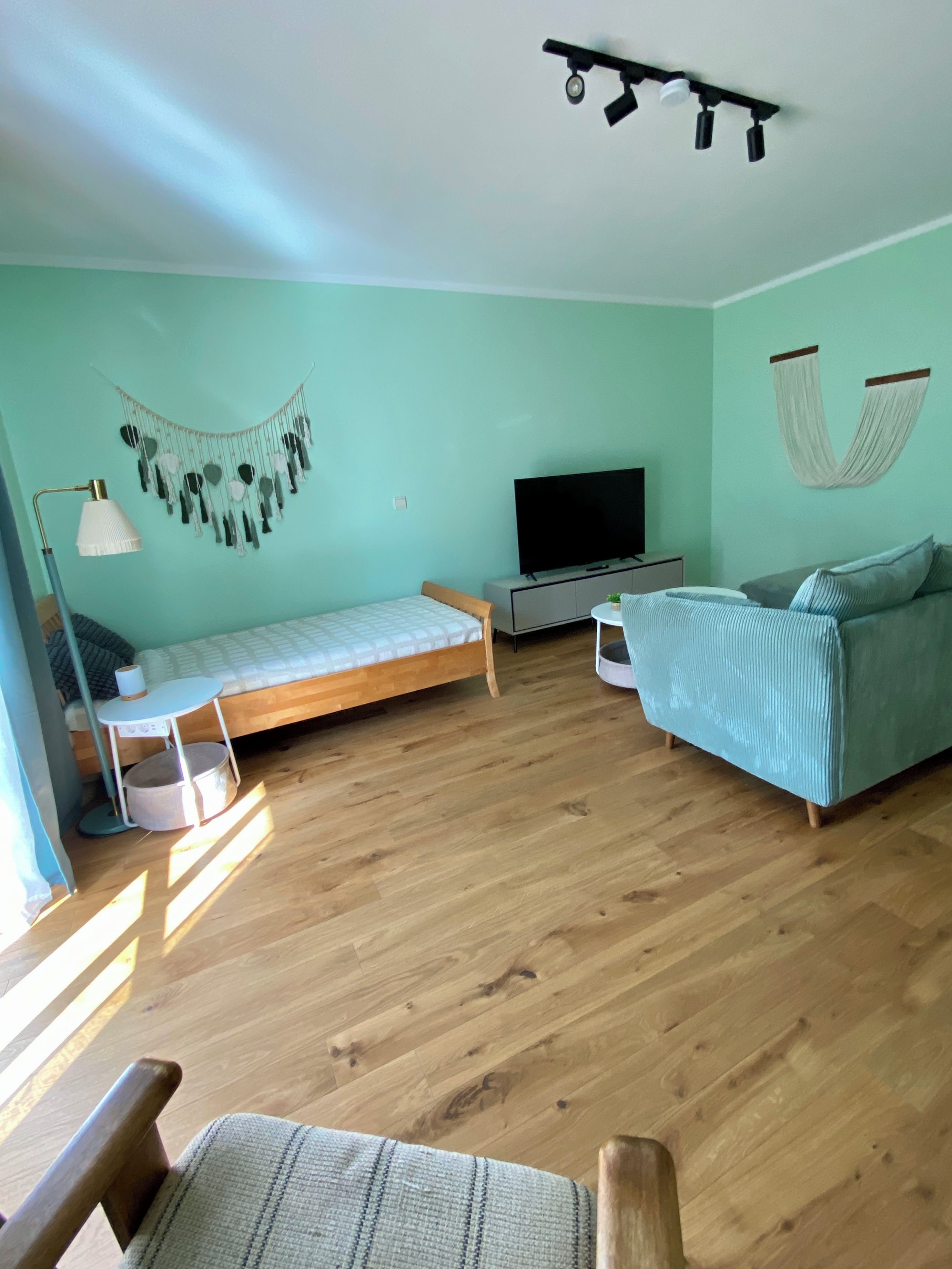 Een kamer met een bed, een bank, een televisie en een hangstoel.