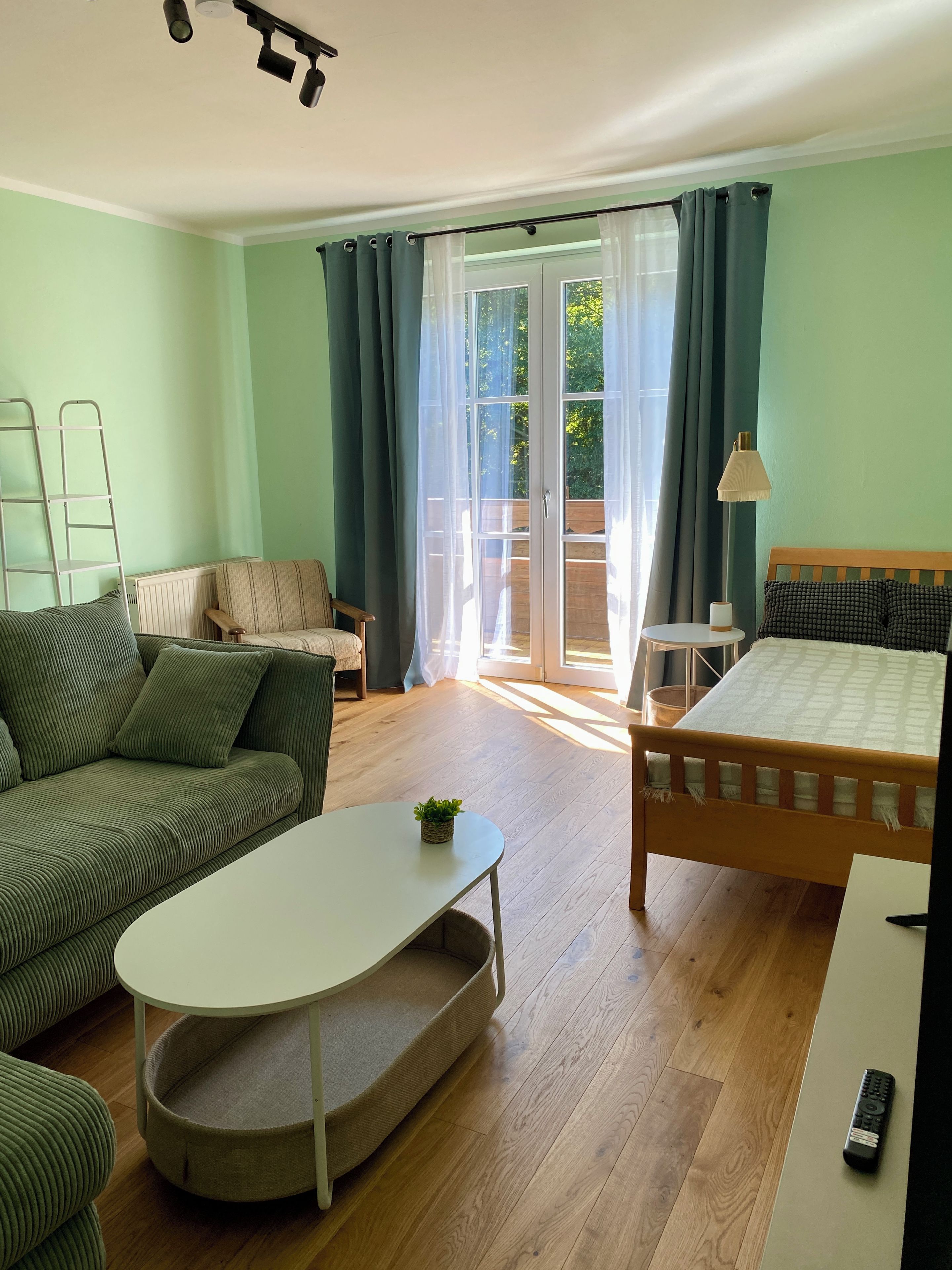 A room with a bed, a sofa, a small table, and a window with curtains.