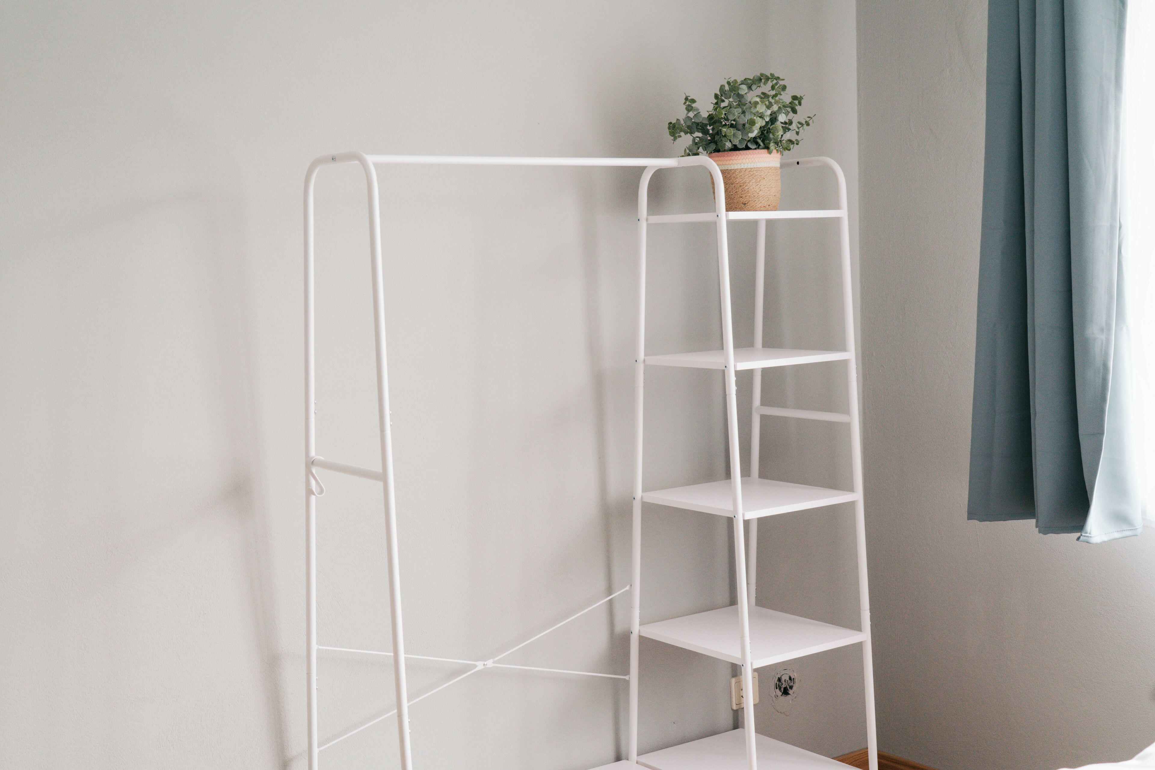 Een witte metalen plank met een plant erop, tegen een effen muur.