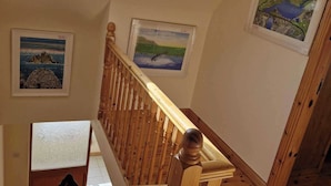 Eine Holztreppe mit Handlauf, die zu einer Zwischenebene mit einer Whiteboard und einem gerahmten Landschaftsbild führt.