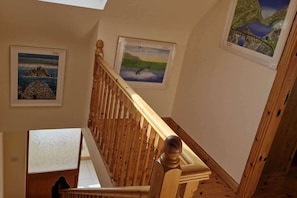 Eine Holztreppe mit Handlauf, die zu einer Zwischenplattform mit einem gerahmten Landschaftsbild führt.