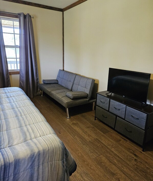 A bedroom with a bed, a sofa, a TV, and a dresser. - Cozy 4-bedroom cabin with WiFi, AC in brilliant Flat Rock (Flat Rock)