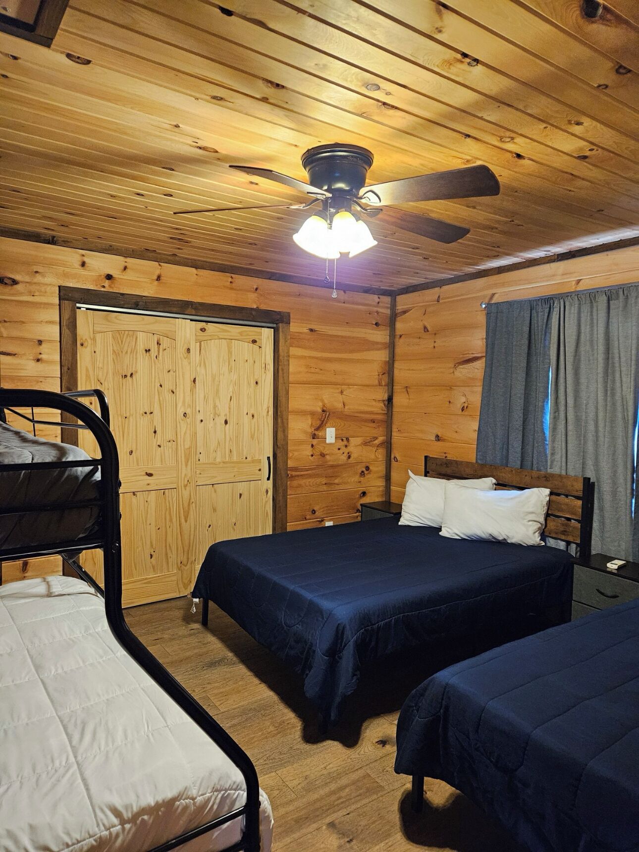 Une chambre de style cabane avec deux lits superposés, un ventilateur de plafond et une porte en bois.