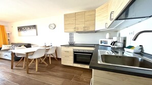 Una cocina moderna con armarios de madera, un comedor con mesa y sillas, un microondas, una cafetera y un reloj en la pared.