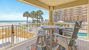 A balcony with a view of the beach and palm trees, a pool, and a building with balconies. - 🏖️Direct Ocean Views-Private Stairs to Beach + Pool-Atlantic Villas 101🏖️ (New Smyrna Beach)