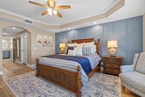 Une chambre à coucher avec un lit en bois, deux tables de chevet avec des lampes, un tapis à motifs et un ventilateur de plafond.