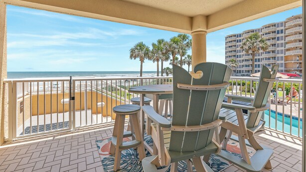 A balcony with a view of the beach and ocean, wooden chairs, and a pool. - 🏖️Direct Ocean Views-Private Stairs to Beach + Pool-Atlantic Villas 101🏖️ (New Smyrna Beach)