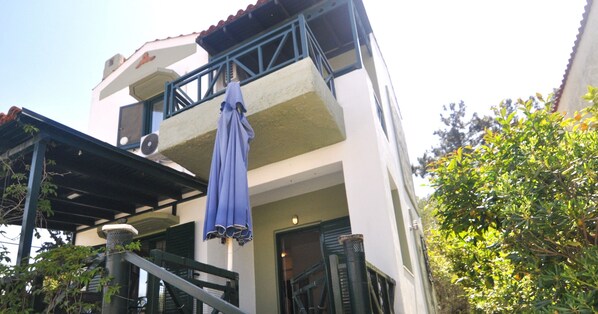 Un edificio de dos plantas con un balcón, una zona de estar al aire libre cubierta y una escalera.