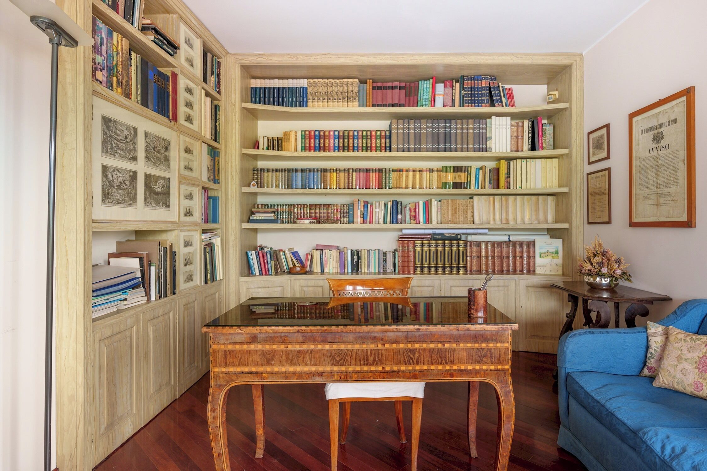 Une pièce avec un bureau en bois, des étagères à livres, un canapé bleu et un document encadré accroché au mur.