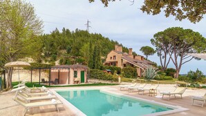 A swimming pool with lounge chairs, a pergola, and a view of a hillside house. - Villa Lia 10, Emma Villas (Roccafluvione)