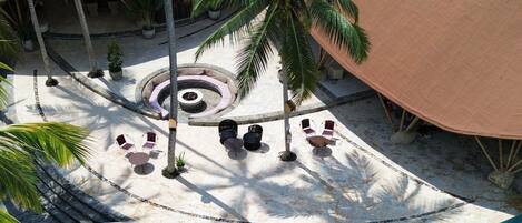 A resort pool area with a clear blue pool, surrounded by palm trees and covered seating areas.