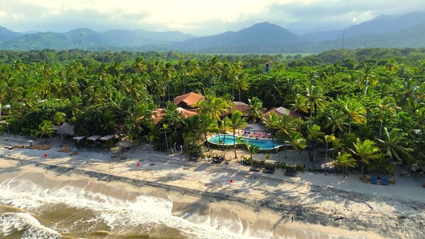 A beach resort with a swimming pool surrounded by palm trees and a view of distant mountains. - Masaya Tayrona & Beach Club (Santa Marta)