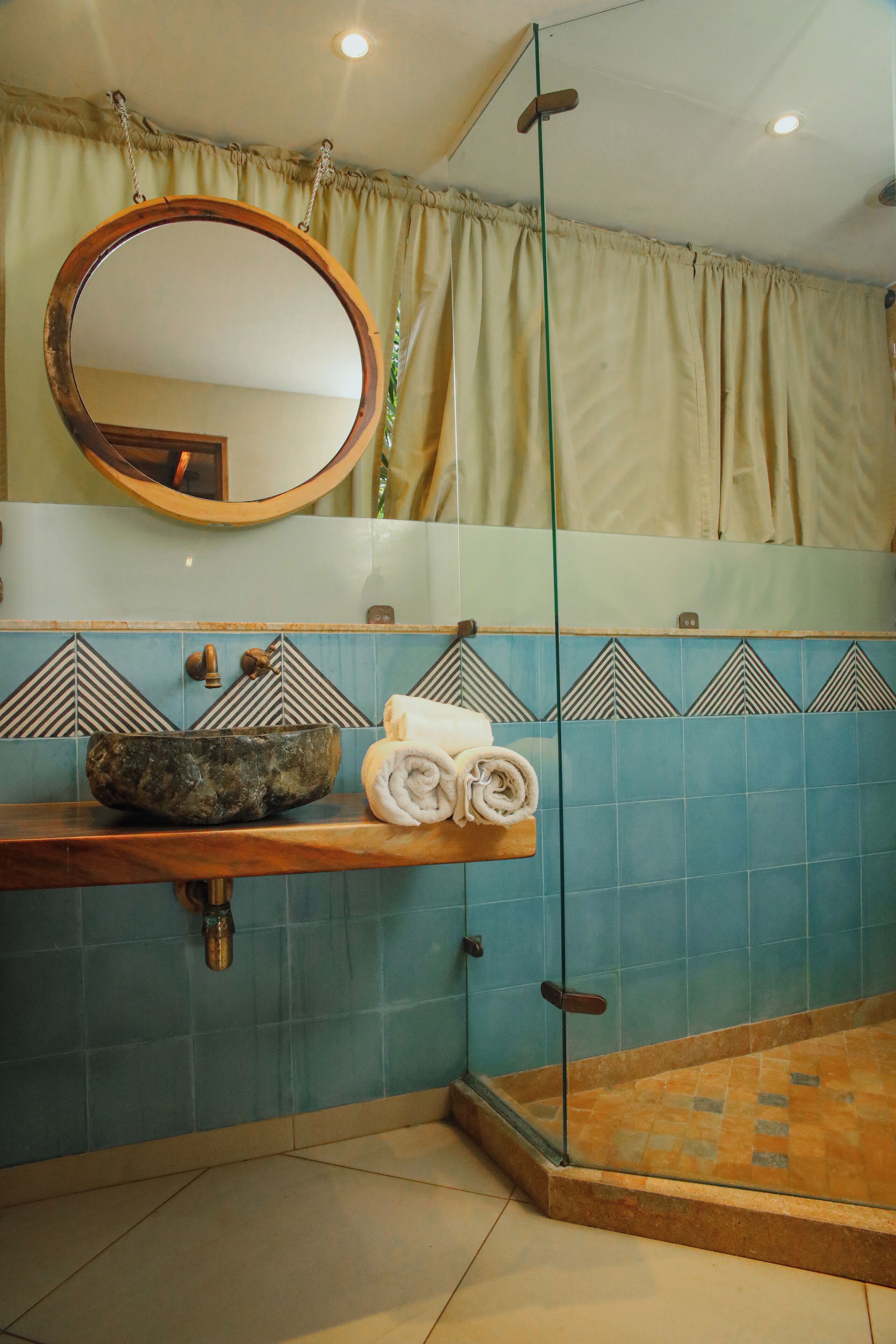 A bathroom with a wooden vanity, a round mirror, a bowl sink, and a glass-enclosed shower area.