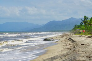A beach with waves, a flag, and mountains in the background. - Masaya Tayrona & Beach Club (Santa Marta)