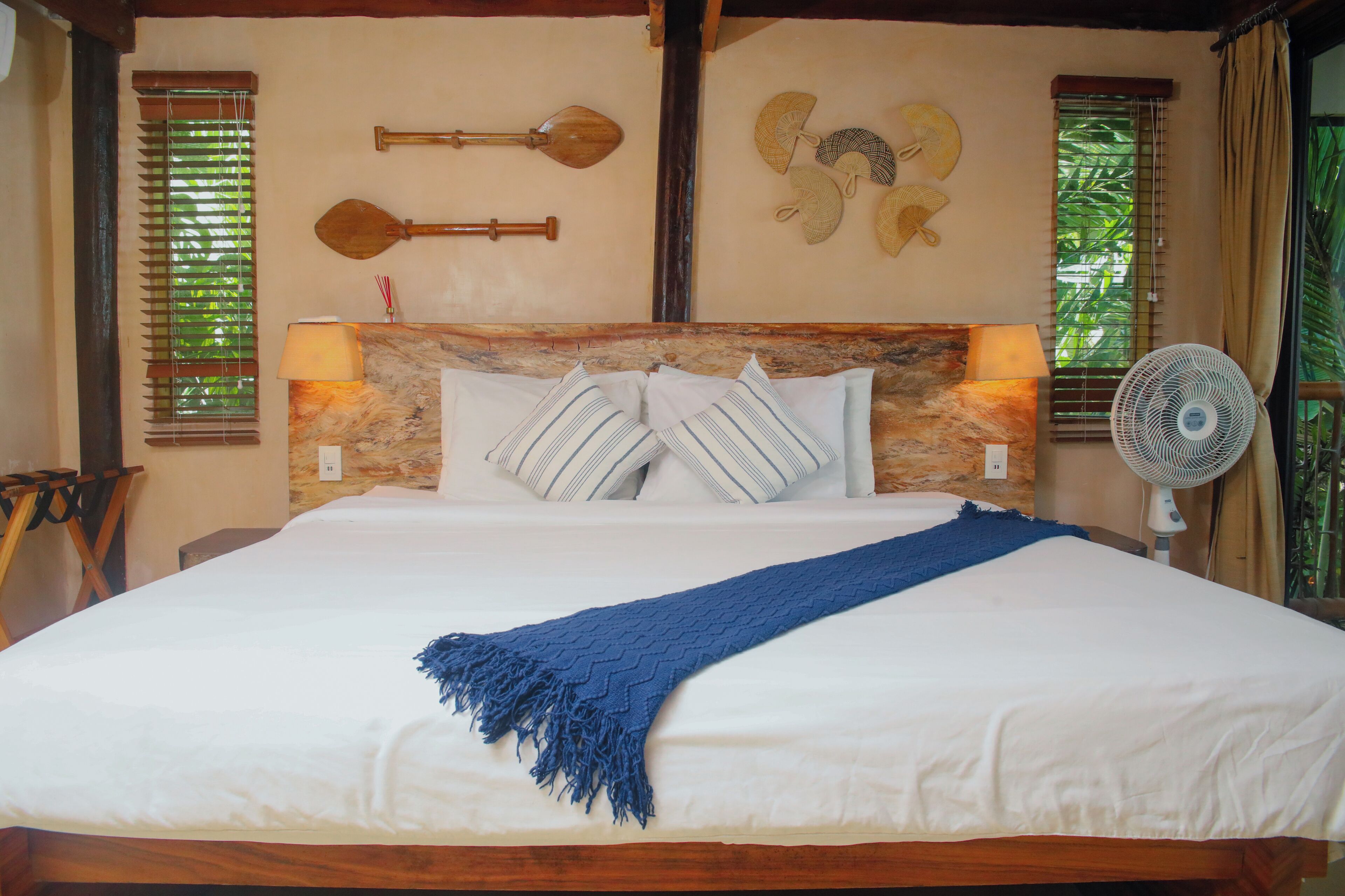A neatly made bed with a blue throw blanket, two wall-mounted fans, and traditional wall decor.