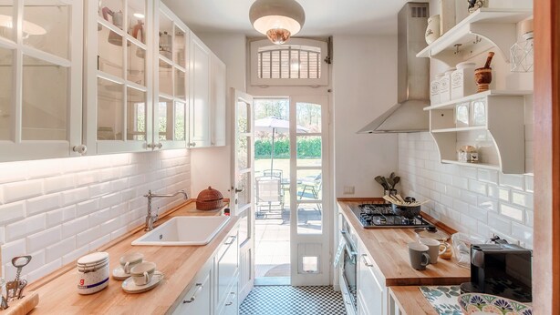 Une cuisine avec des meubles blancs, un carrelage à motifs et une vue sur l’extérieur.
