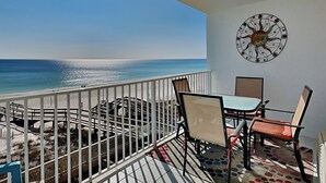 A balcony with a view of the ocean, a table with chairs, and a decorative wall piece. - Perdido Skye #24 by Southern Vacation Rentals (Pensacola)
