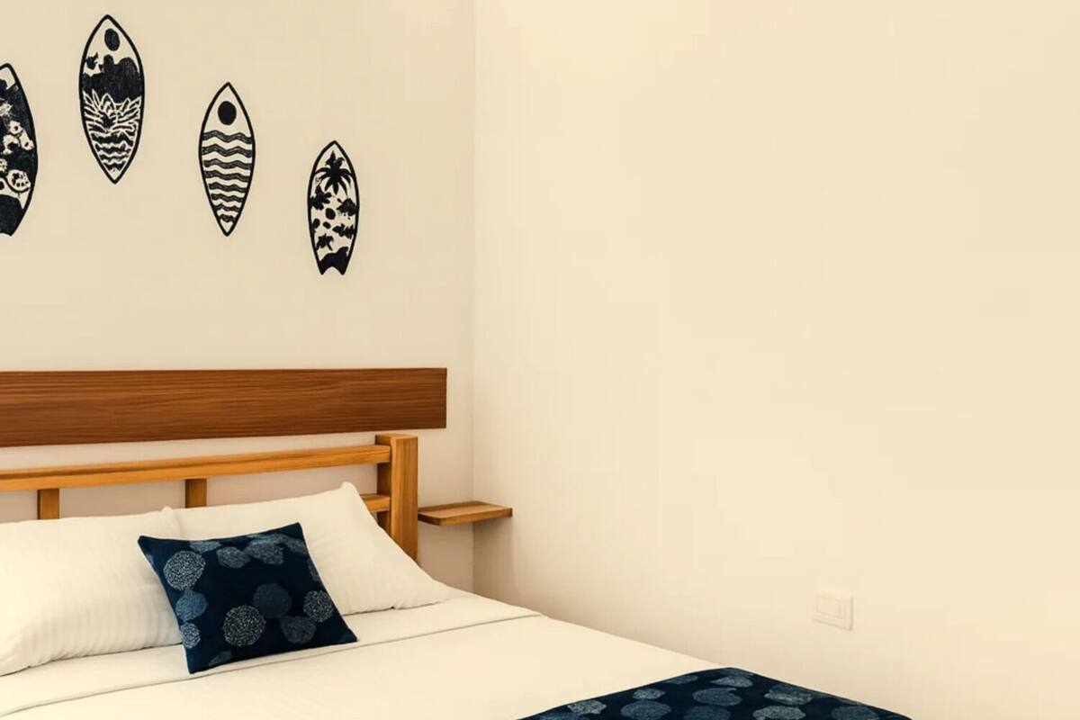 A bed with a wooden frame, white bedding, and a dark blue patterned throw.