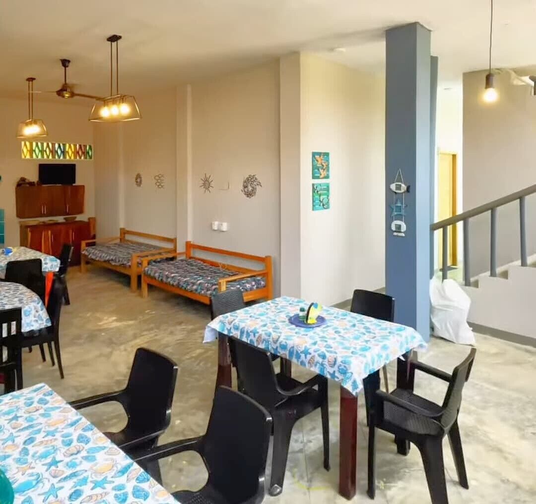 A dining area with tables and chairs, a staircase, and a bed in the background.