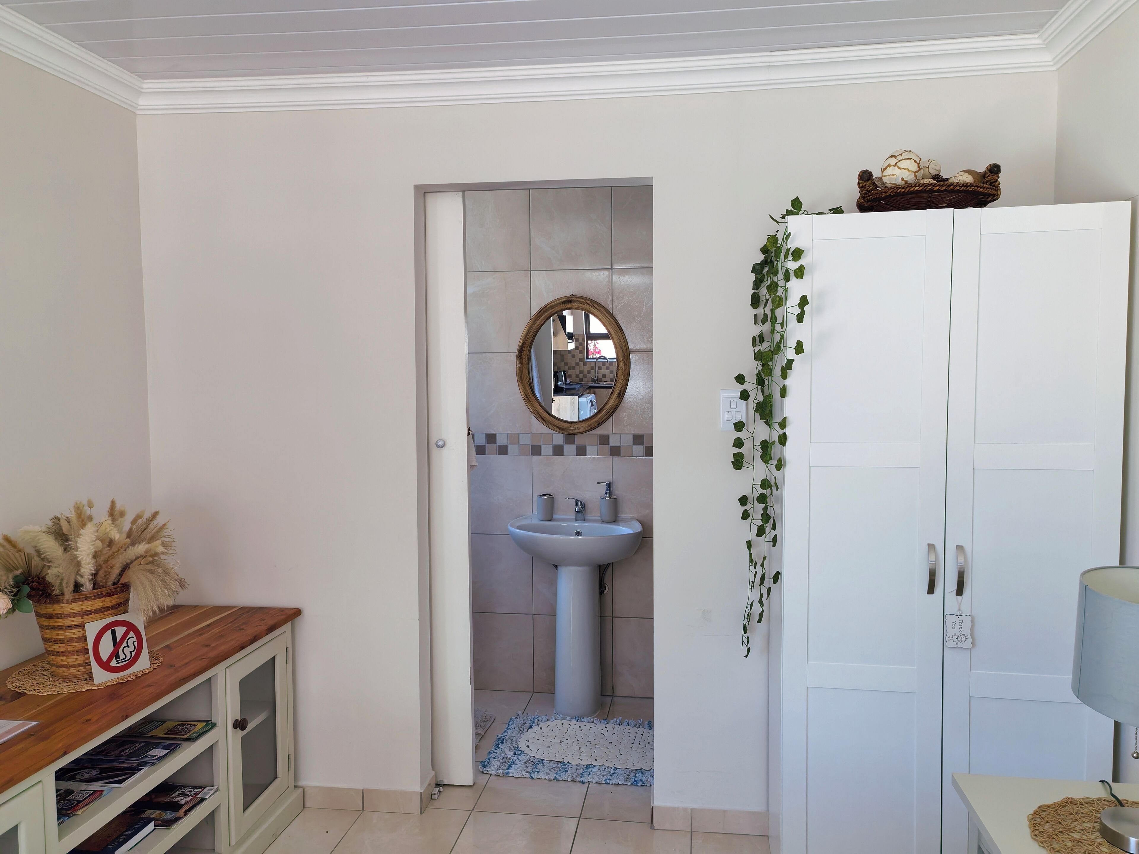 Een badkamer met een wit wastafel, een spiegel en een deur naar een andere kamer.