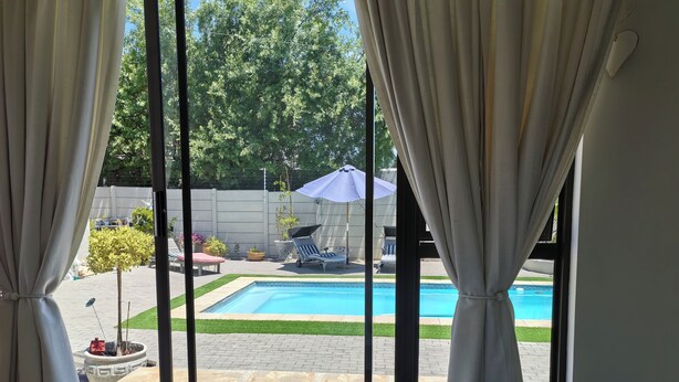 Un dormitorio con vista a un patio trasero que cuenta con una piscina, mobiliario exterior y un pequeño árbol.