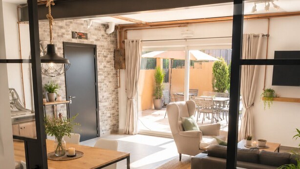 A modern living room with a sofa, dining table, and chairs, a kitchen area with a stove, and a view of the outdoor patio. - Loft with Pool near Valencia and the Ricardo Tormo Circuit (VC)