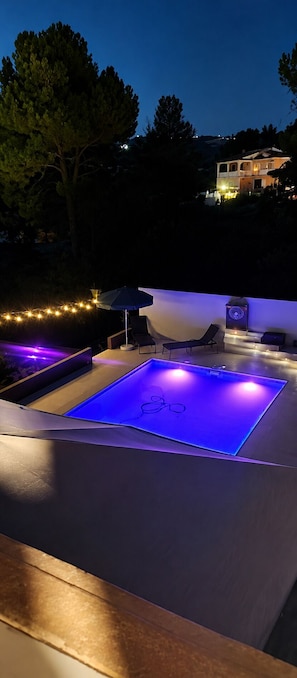 An outdoor swimming pool area with a poolside lounge and string lights.
