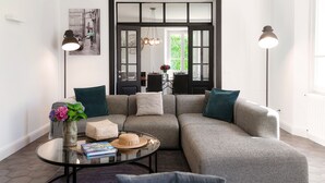 A modern living room with a sectional sofa, a glass coffee table, and a dining area visible through an open door.