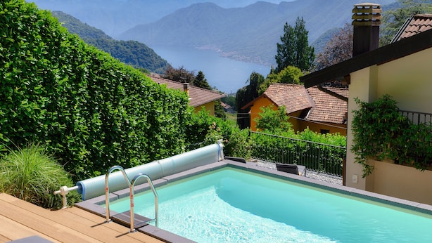 A pool with a view of mountains and a lake, surrounded by greenery and buildings.