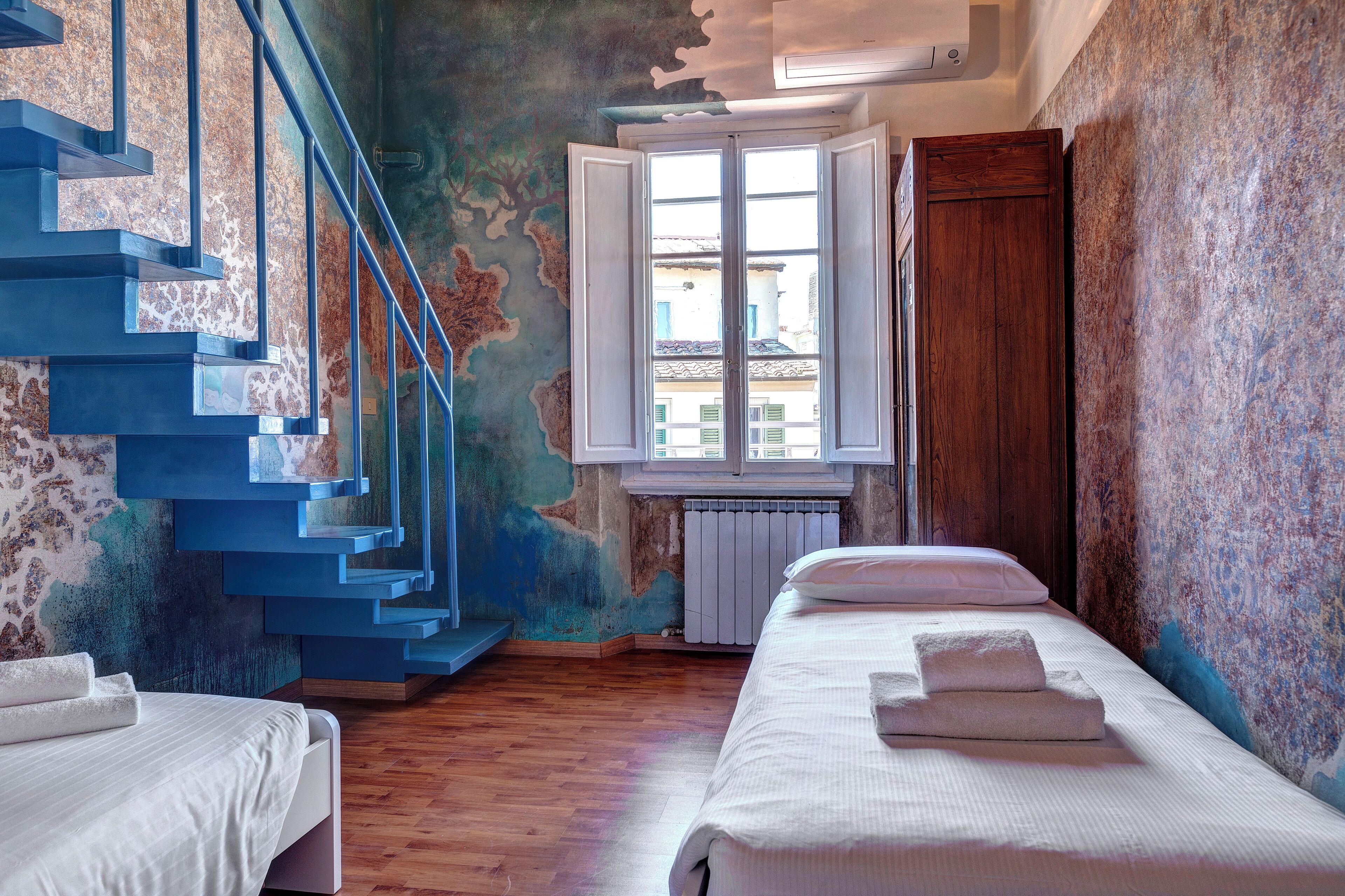 A bedroom with a wooden staircase, a window with white shutters, and a radiator.