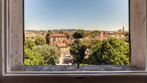 Blick aus einem Fenster auf eine Stadt mit Gebäuden, Bäumen und einer entfernten Hügelkulisse.